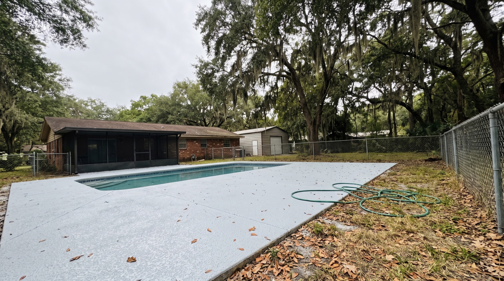 Resurfaced light-grey textured pool deck at a Green Cove Springs home shaded by mature live oaks