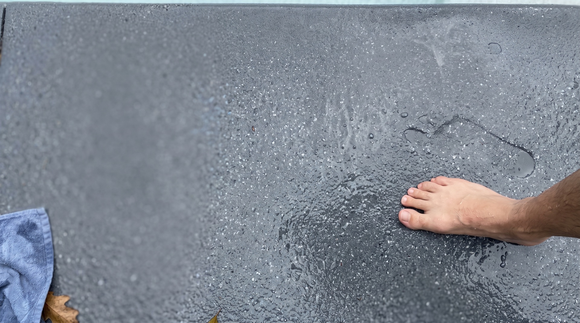Bare foot standing on a wet, textured slip-resistant concrete coating beside a Florida pool deck, showing the aggregate grip finish